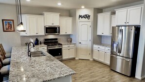 A modern kitchen with white cabinets, stainless steel appliances, and a granite countertop. - Estrella Skies Backyard Delight, Stunning Pool 4 Beds 2 Bath, Vacation Retreat (Goodyear)