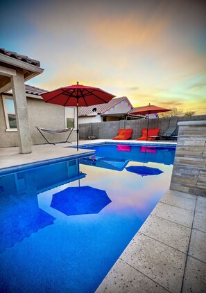 A swimming pool with a hexagonal pattern on the floor, surrounded by lounge chairs and umbrellas. - Estrella Skies Backyard Delight, Stunning Pool 4 Beds 2 Bath, Vacation Retreat (Goodyear)