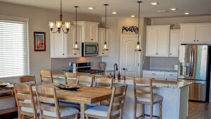 A modern kitchen with white cabinets, a central island, and a dining area with wooden chairs. - Estrella Skies Backyard Delight, Stunning Pool 4 Beds 2 Bath, Vacation Retreat (Goodyear)