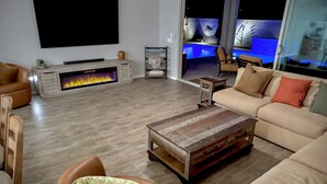 A living room with a fireplace, sofa, coffee table, and a TV mounted on the wall. - Estrella Skies Backyard Delight, Stunning Pool 4 Beds 2 Bath, Vacation Retreat (Goodyear)