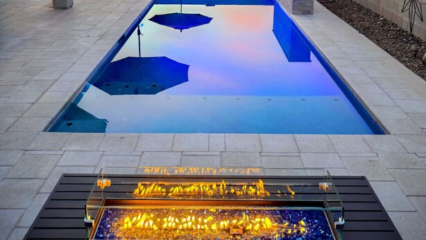 A swimming pool with a fire feature, lounge chairs, and a patio umbrella. - Estrella Skies Backyard Delight, Stunning Pool 4 Beds 2 Bath, Vacation Retreat (Goodyear)