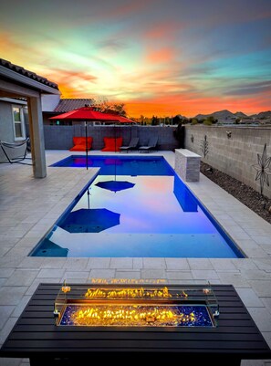 A swimming pool with a fire feature, lounge chairs, and a patio umbrella. - Estrella Skies Backyard Delight, Stunning Pool 4 Beds 2 Bath, Vacation Retreat (Goodyear)