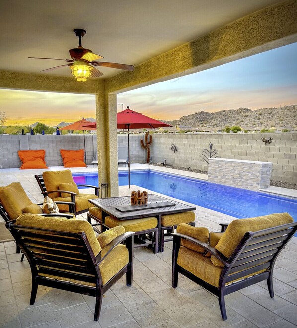 A poolside area with a table and chairs, a ceiling fan, and a view of a mountainous landscape. - Estrella Skies Backyard Delight, Stunning Pool 4 Beds 2 Bath, Vacation Retreat (Goodyear)