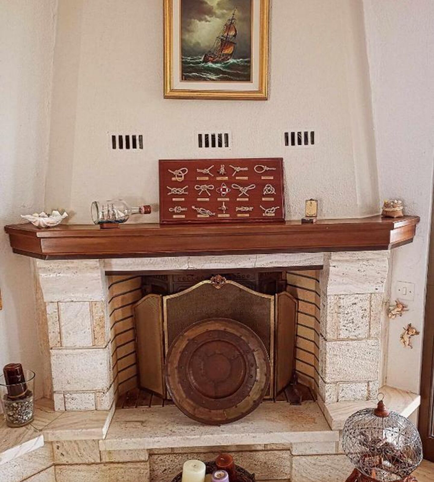A fireplace with a framed collection of nautical knots and a ship model.