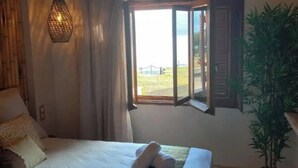 Ein Schlafzimmer mit Bett, einer Pendelleuchte, einem Fenster mit Vorhängen und einer Topfpflanze.
