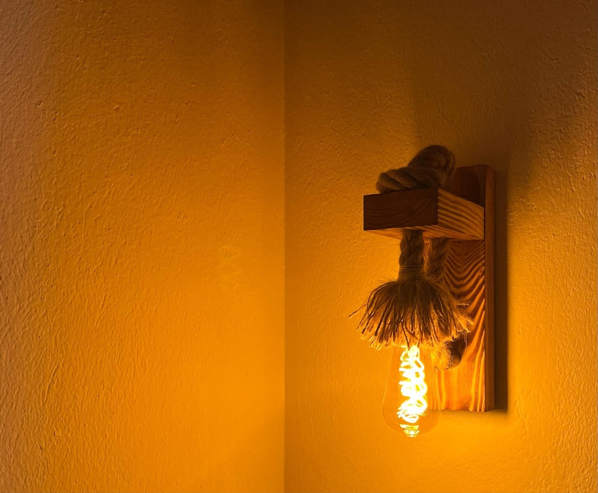 A wall-mounted light fixture with a rustic design, featuring a wooden block and a hanging element.