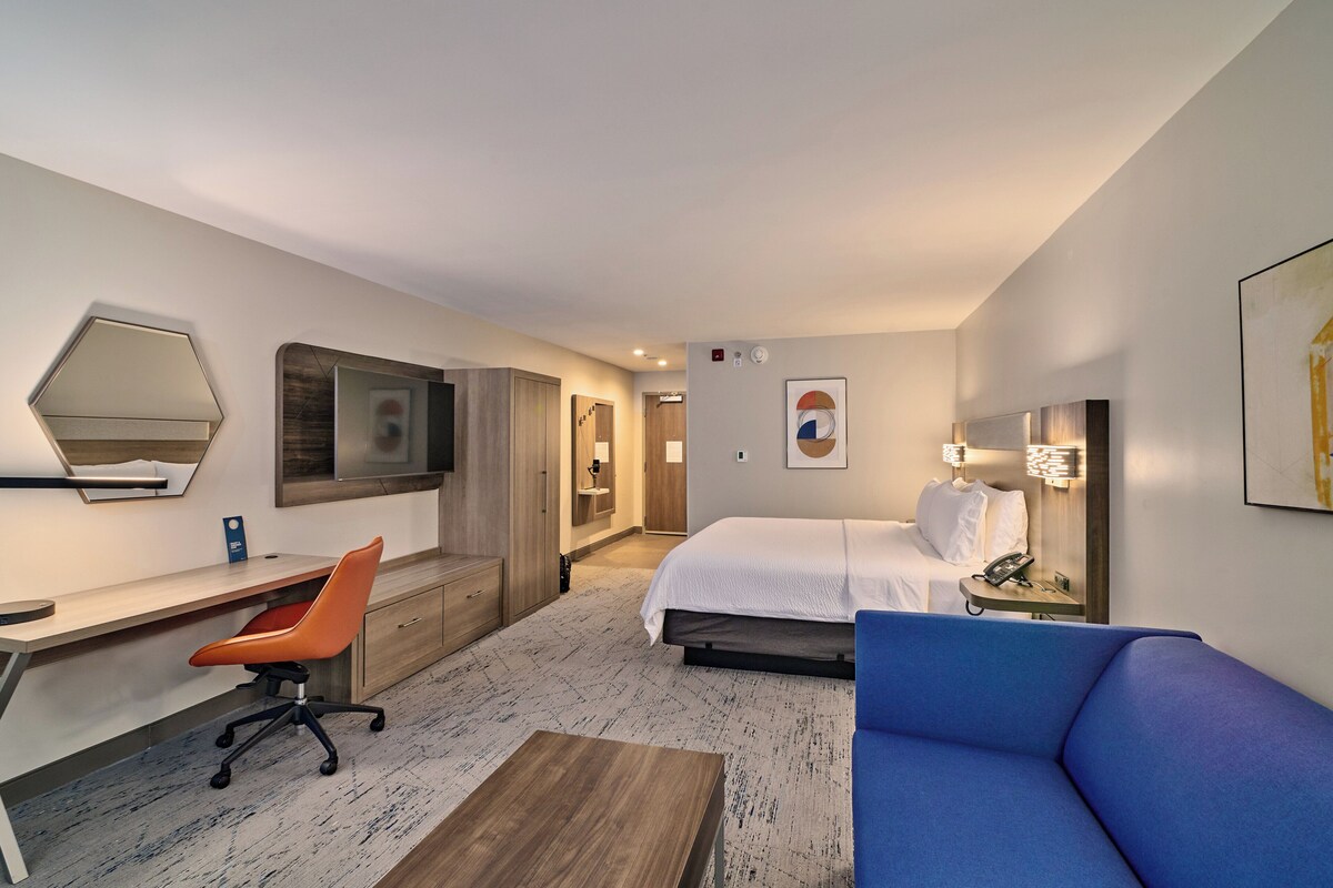 A hotel room with a bed, a desk, a chair, a sofa, and a TV.
