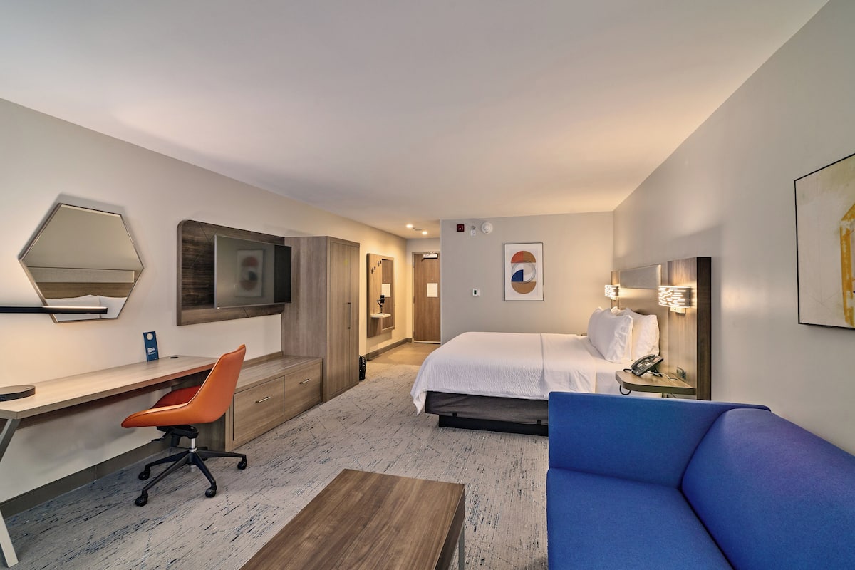 A hotel room with a bed, a desk, a chair, a sofa, and a TV.