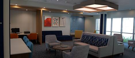 A modern hotel lobby with a reception desk, seating area, and large windows.