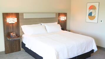 Een keurig opgemaakt bed in een hotelkamer, met een houten hoofdbord, nachtlampjes en een aan de muur hangend kunstwerk.