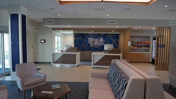 A modern lobby with seating areas, a reception desk, and a visible kitchenette.