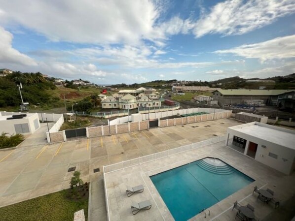 A rooftop pool area with lounge chairs and a swimming pool, surrounded by buildings and a hilly landscape.