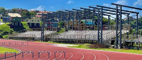 A running track with hurdles, a blue metal structure, and houses in the background.