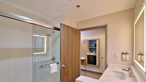 A modern bathroom with a glass shower enclosure, a wooden door, and a white sink with a large mirror.