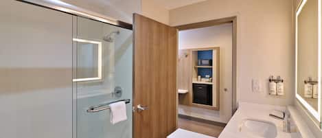 A modern bathroom with a glass shower enclosure, a wooden door, and a white sink with a large mirror.