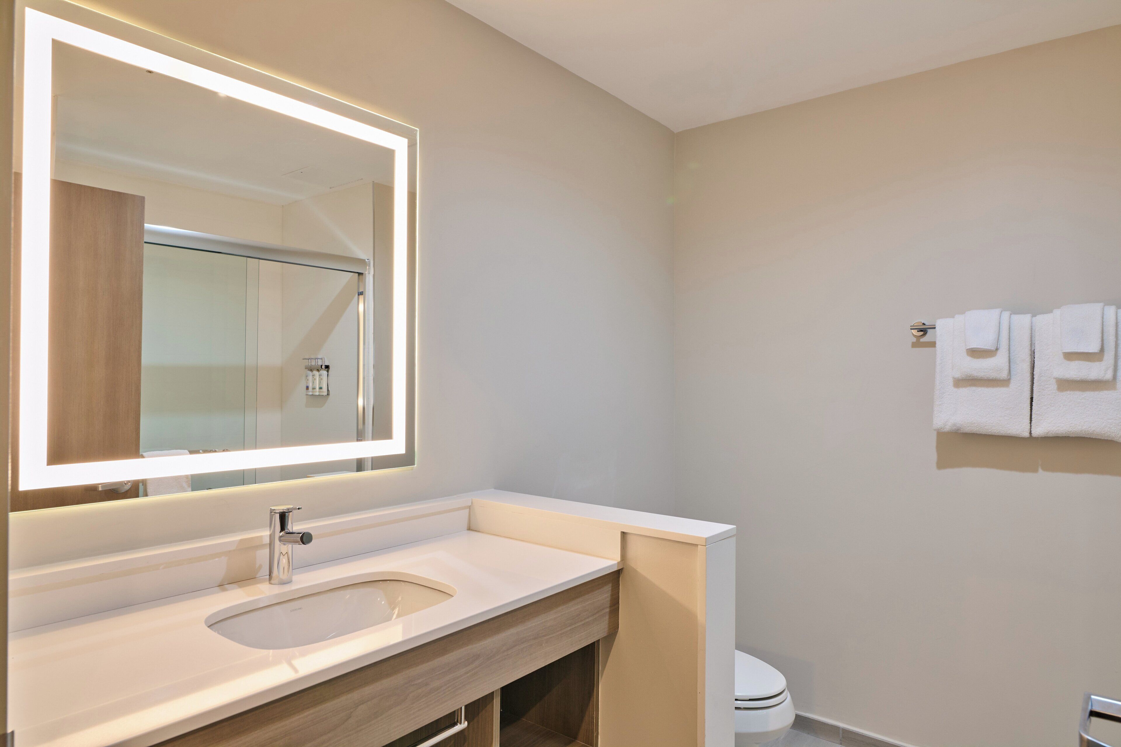 A modern bathroom with a large mirror, a sink, and a toilet.