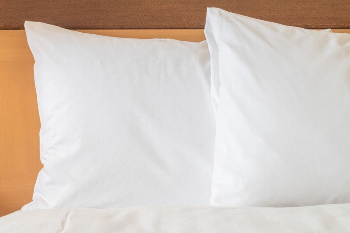 A bed with white bedding and pillows against a wooden headboard.
