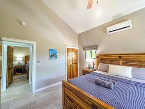 A bedroom with a bed, a nightstand, a wall-mounted air conditioner, and a door leading to another room.