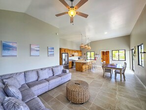 A spacious living area with a sofa, a dining table with chairs, a kitchen with wooden cabinets, and a ceiling fan.