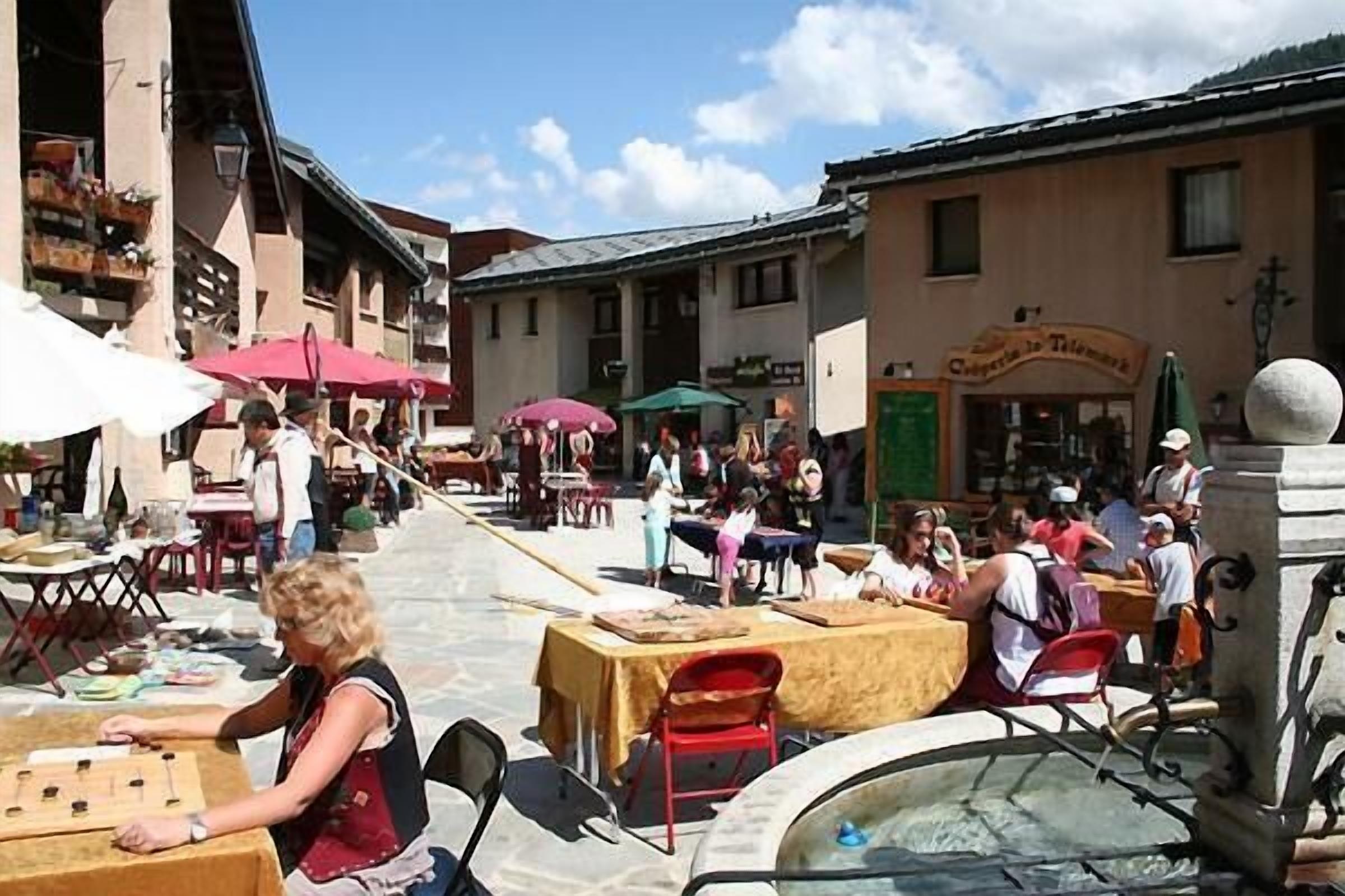 Ein Straßencafé mit Tischen, Stühlen, einer Fontäne und Gebäuden im Hintergrund.