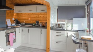 A modern kitchen with white cabinets, a wooden ceiling, and a window with a view. - Babbling Brook Lodge (Trawsfynydd)