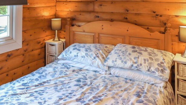 A wooden cabin-style room with a bed, two bedside lamps, and a window. - Babbling Brook Lodge (Trawsfynydd)