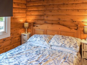 Una habitación tipo cabaña de madera con una cama, dos lámparas de noche y un ventanal.