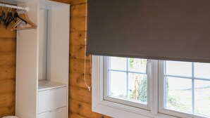 A room with wooden paneling, a white wardrobe, a window with a white blind, and a view of greenery outside. - Babbling Brook Lodge (Trawsfynydd)