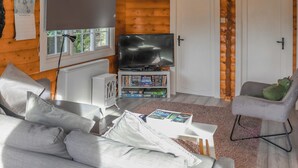 A log cabin interior with a sofa, a television, a bookshelf, and a plush toy. - Babbling Brook Lodge (Trawsfynydd)