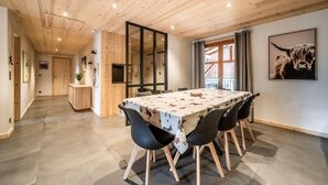 A dining area with a long table, black chairs, wooden ceiling, and a large window with curtains. - 1st floor, view village, balcony, fireplace or stove, parking, tv, ski locker, 97m², Morzine (Morzine)