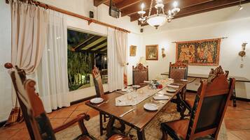 A dining room with a wooden table set for six, surrounded by ornate chairs, a chandelier, and a large tapestry on the wall.