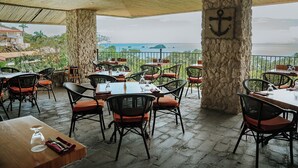 An outdoor dining area with stone pillars, tables, and chairs. - Vista Suites at Parador (Quepos)
