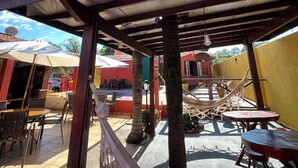 An outdoor patio area with wooden tables and chairs, a hammock, and a pool. - Recanto da Vó Ziza (Brotas)