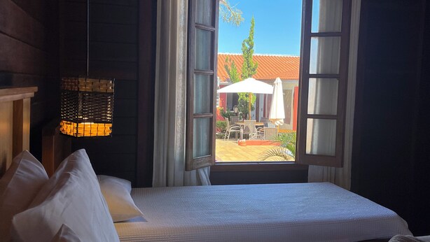A bedroom with a large bed, a window with curtains, a hanging light fixture, and a view of the outside. - Recanto da Vó Ziza (Brotas)