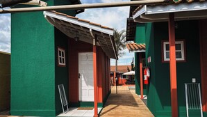 A narrow alleyway with green and red buildings, a white door, and a fire extinguisher on the right. - Recanto da Vó Ziza (Brotas)
