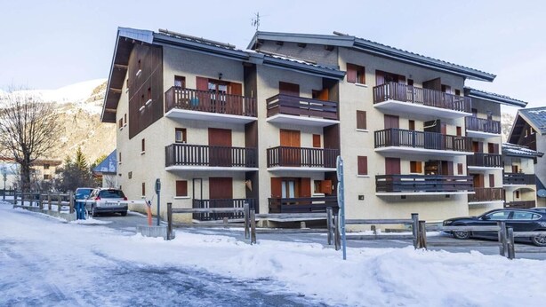 Un hotel a più piani con balconi, una pista da sci sullo sfondo e terreno innevato.