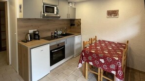 Una cucina compatta con forno a microonde, piano cottura e lavello, un tavolo da pranzo con tovaglia fantasia e un piccolo armadietto.
