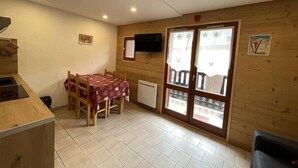 Una stanza accogliente e piccola con arredamento in legno, un tavolo da pranzo con sedie, un televisore montato a parete e una porta scorrevole in vetro che dà su uno spazio esterno.