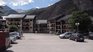 Un hotel con diversi balconi, un parcheggio e montagne sullo sfondo.
