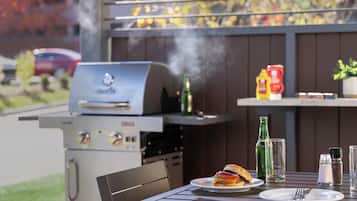 Una parrilla con hamburguesa en un plato, una botella de cerveza y condimentos sobre una mesa.
