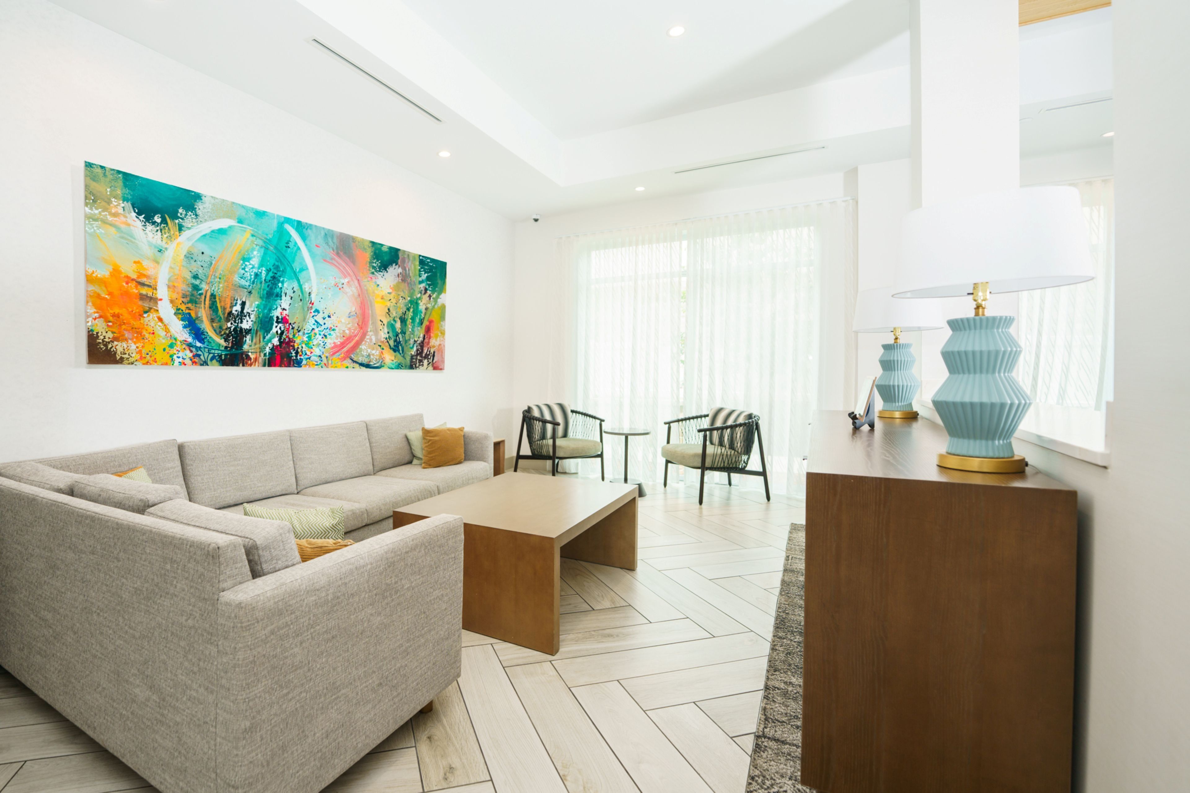 A modern living room with a grey sofa, a wooden coffee table, and a colorful abstract painting on the wall.