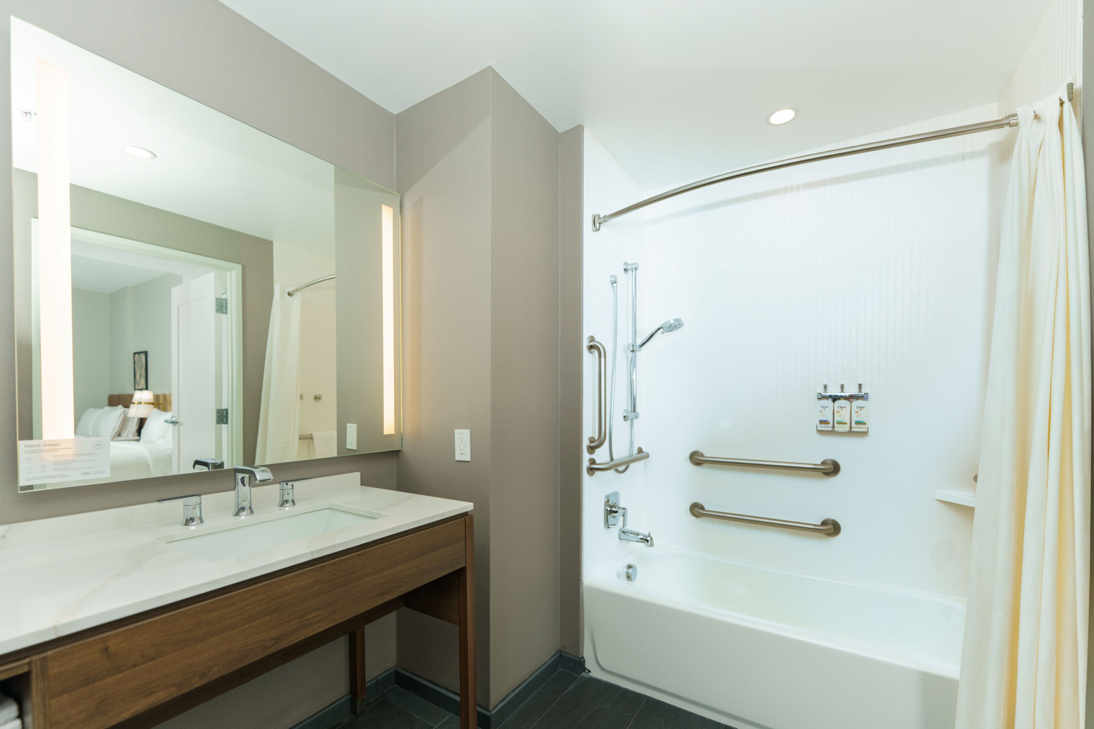 A bathroom with a double sink vanity, a bathtub, and a shower with grab bars.