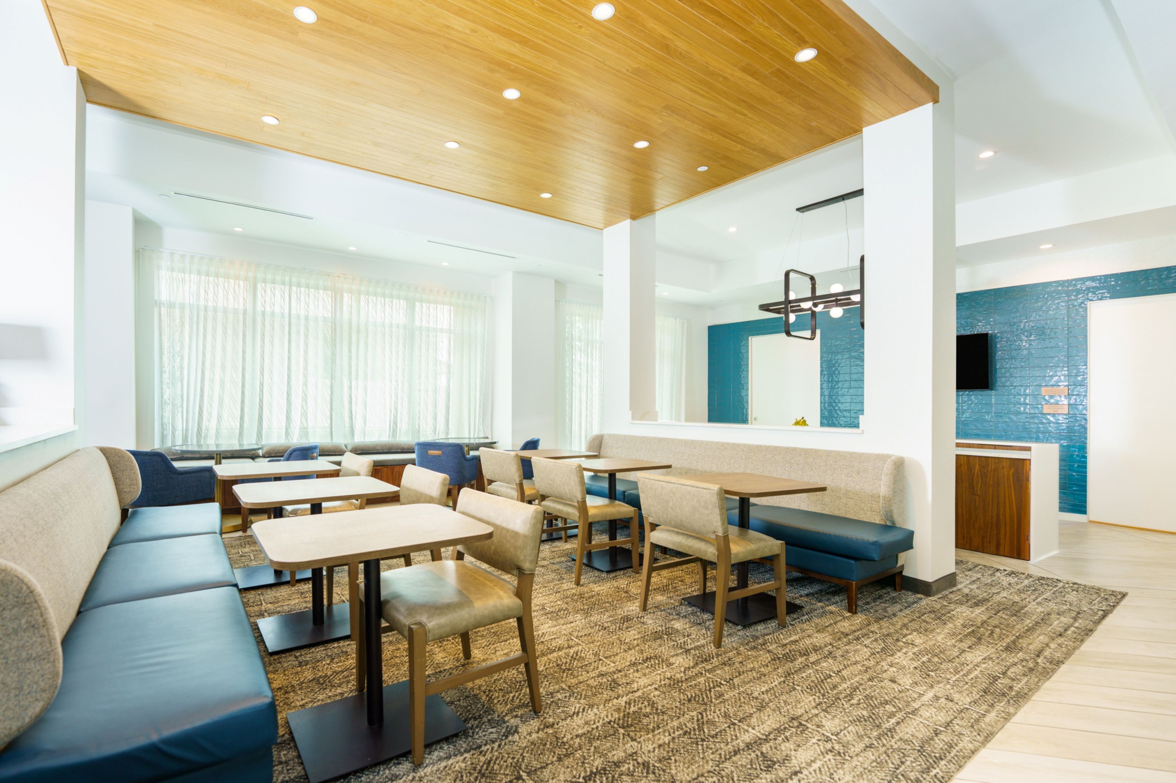 A modern hotel lobby with a seating area, tables, and a kitchen area.