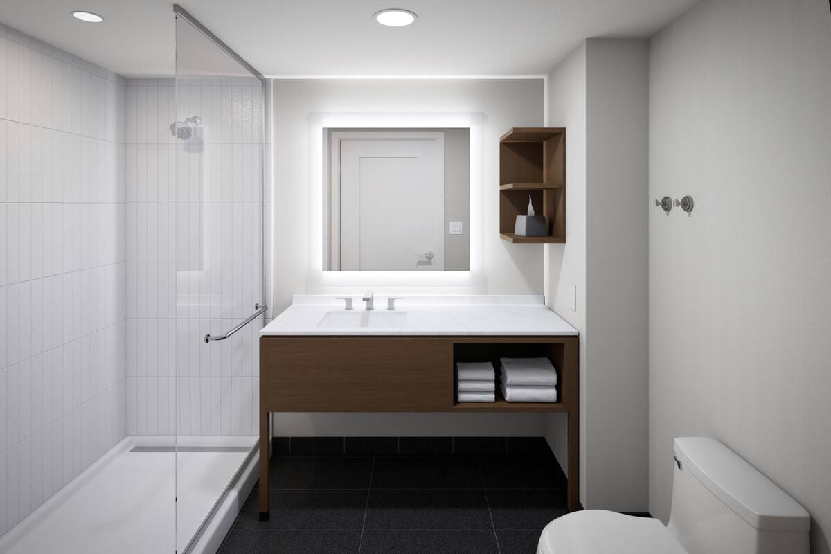 Un bagno moderno con cabina doccia in vetro, lavandino bianco su mobile contenitore in legno e vaso sospeso bianco.