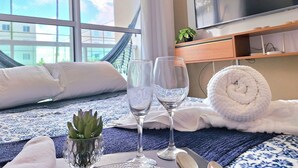 A hotel room with a bed, a TV, a glass of water, a rolled towel, and a small plant on the bedside table. - Palm Village (Ipojuca)