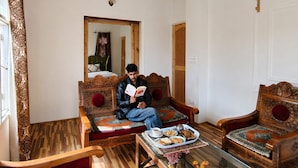 A room with a ceiling fan, a sofa, a coffee table, and a dining table with a tray of food. - Shesh Bagh Boutique Homestay (Srinagar)