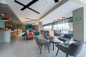 A modern interior with seating areas, a reception desk, and a view through large windows. - avid hotel Queretaro Centro Sur by IHG (Querétaro)