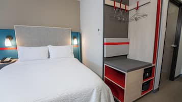 Una habitación de hotel con cama, escritorio con teléfono y armario con detalle rojo.