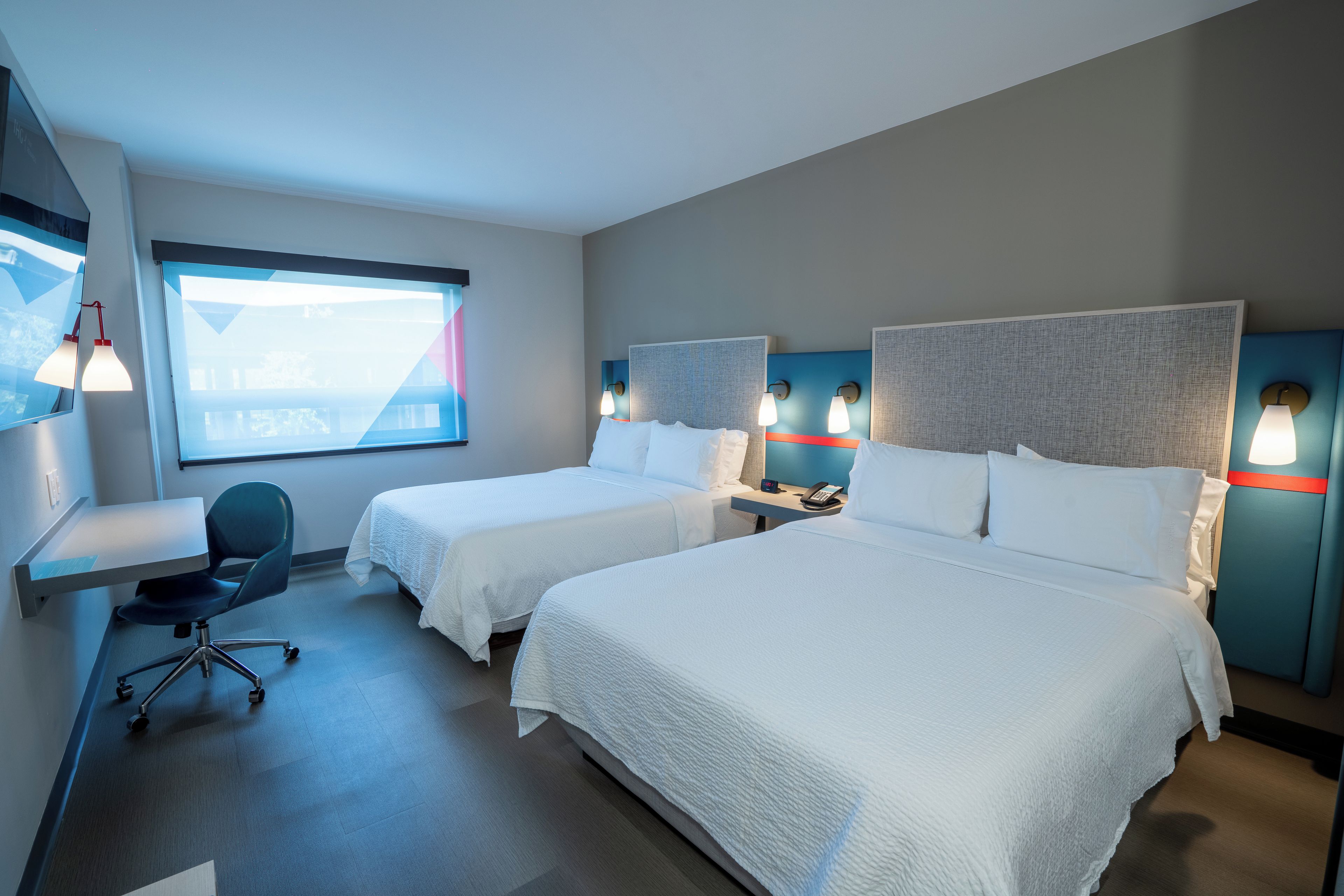 A hotel room with two beds, a desk, and a chair.