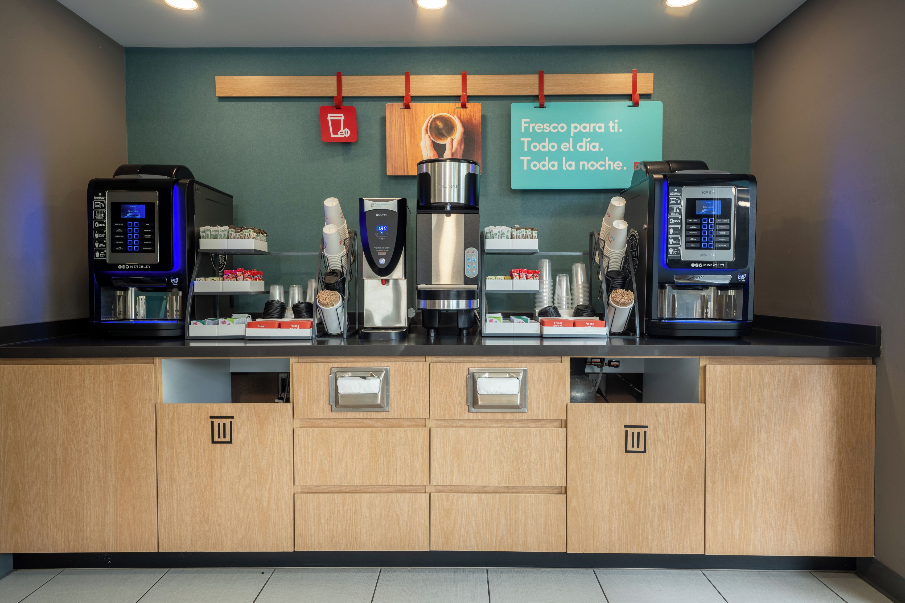 A coffee station with multiple coffee machines and a sign above stating 'Fresh for the day. All the night.'